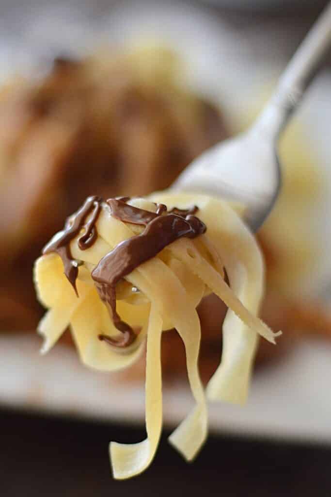 A fork with some fettuccine crepe drizzled with chocolate sauce.