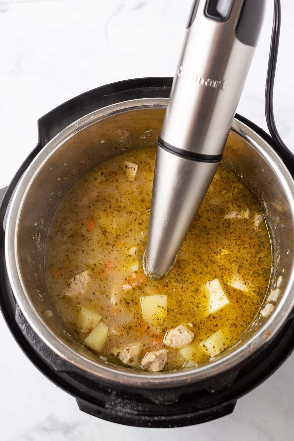 A immersion blender in an instant pot with potato soup.