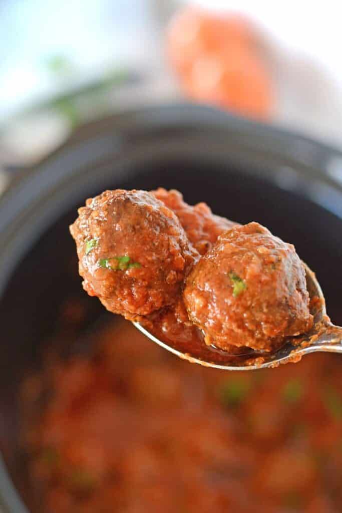 A clode up look on a spoon scooping some meatballs from the slow cooker.