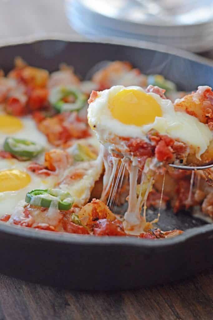 A spoon scooping some potato shakshuka from a skillet.