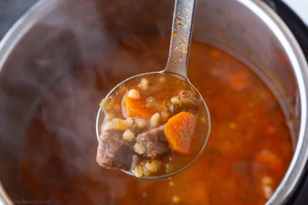 A ladle with some barley soup over an instant pot.
