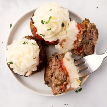 Overhead view of a white plate with meatloaf cupcakes with one cut in half to show texture.