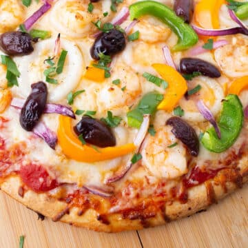 A close up look at a seafood pizza on a wooden surface.