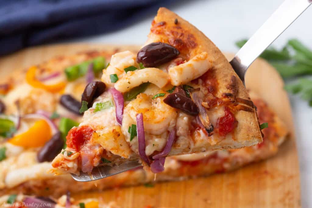 A serving spoon with a slice of seafood pizza.