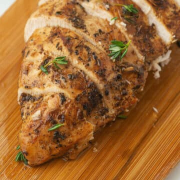 A close up image on a grilled chicken breast on a wooden cutting board.