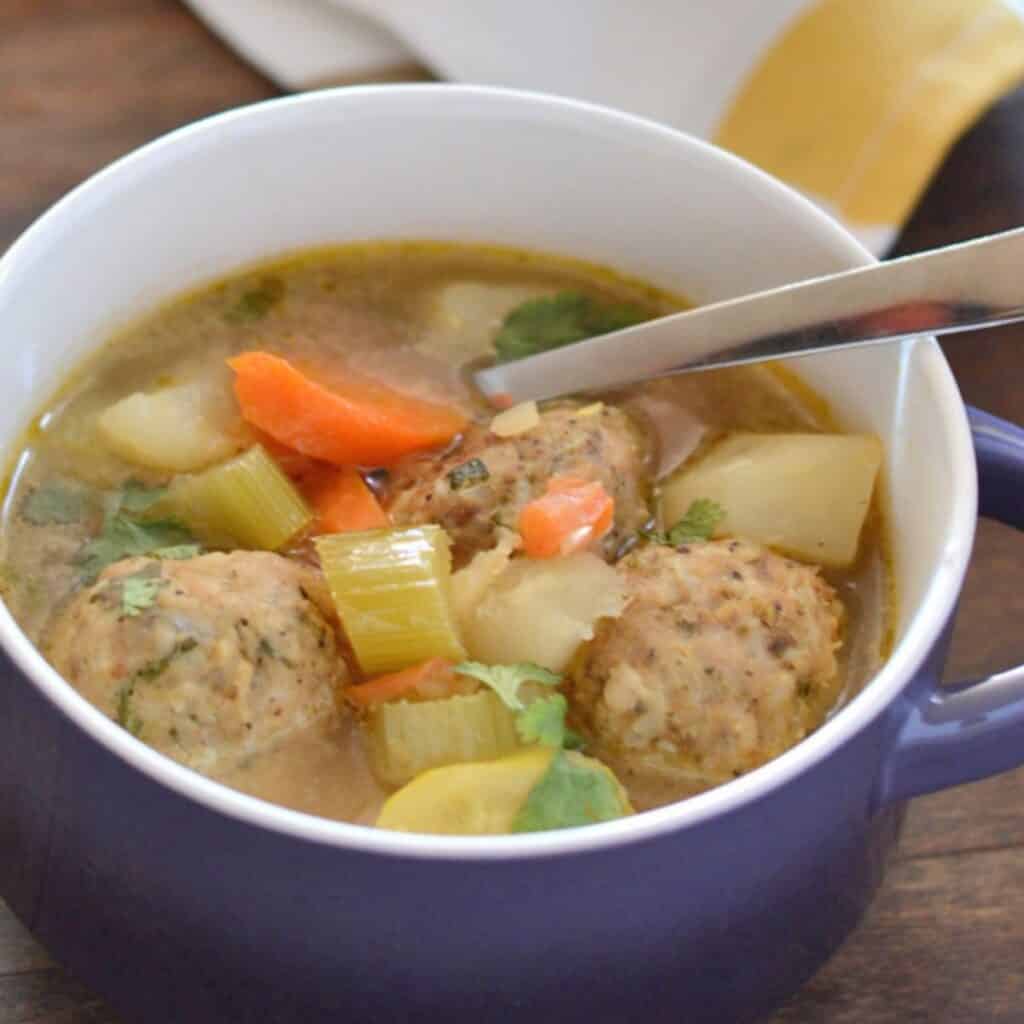 A soup bowl with albondigas soup and a spoon in it.