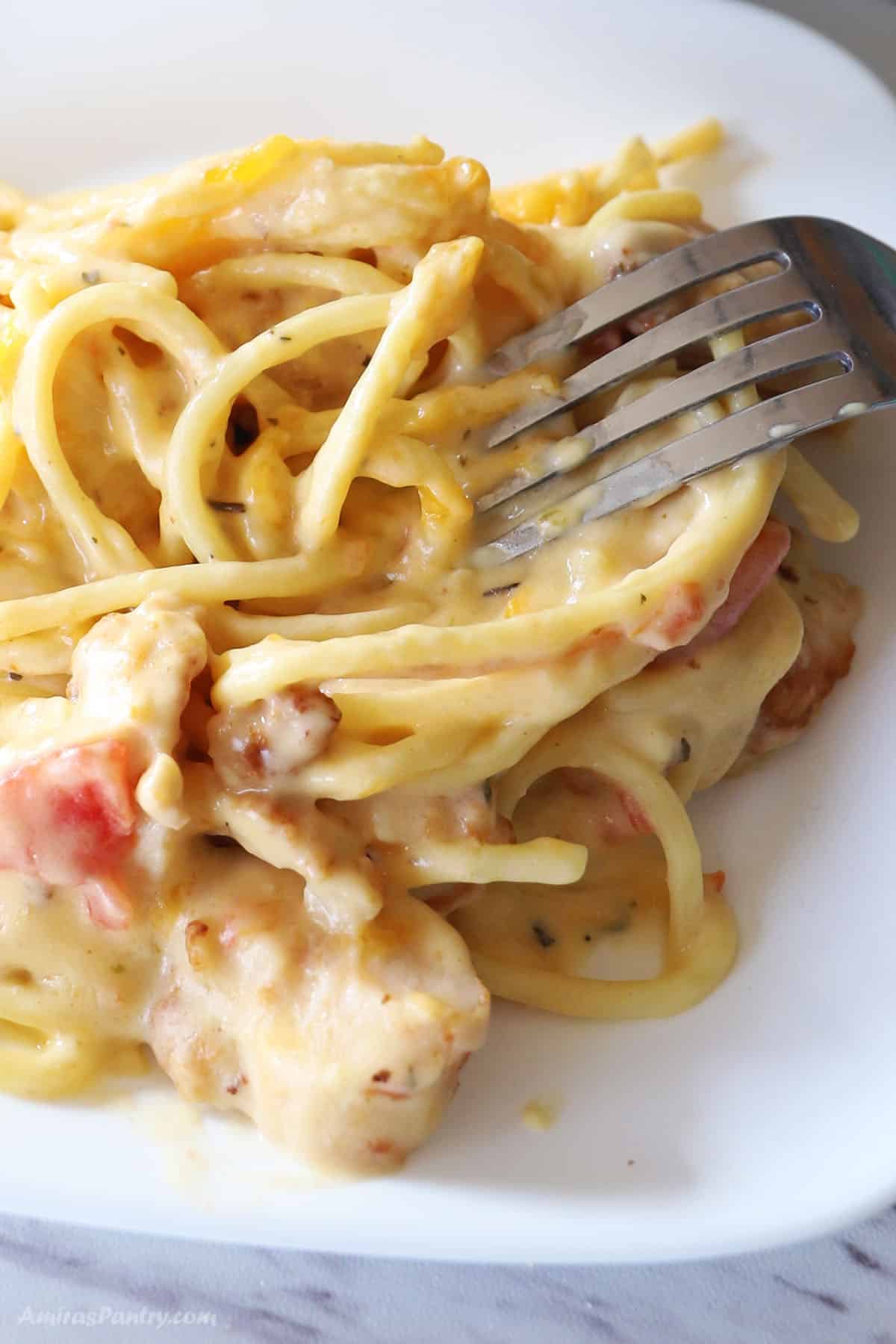 A white plate with chicken spaghetti and a fork in it.
