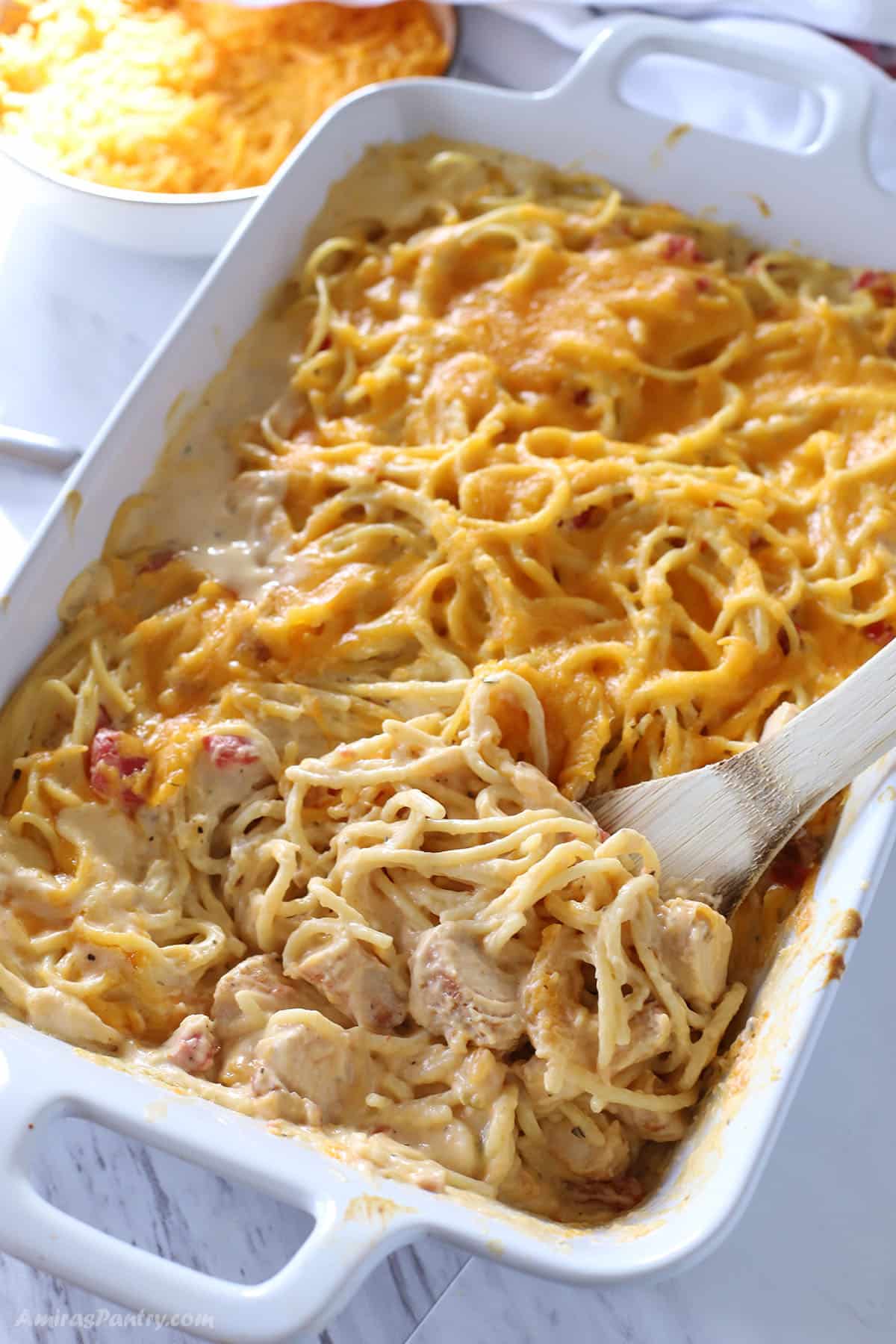 Wooden spoon in a casserole of chicken spaghetti.