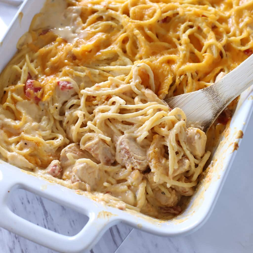 Wooden spoon in a casserole of chicken spaghetti.