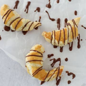 Three cocolate croissants on a white parchment paper.