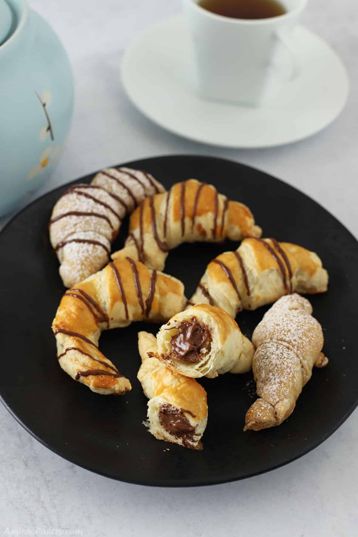 Chocolate croissants on a black serving plate with one cut in half to show melted chocolate.