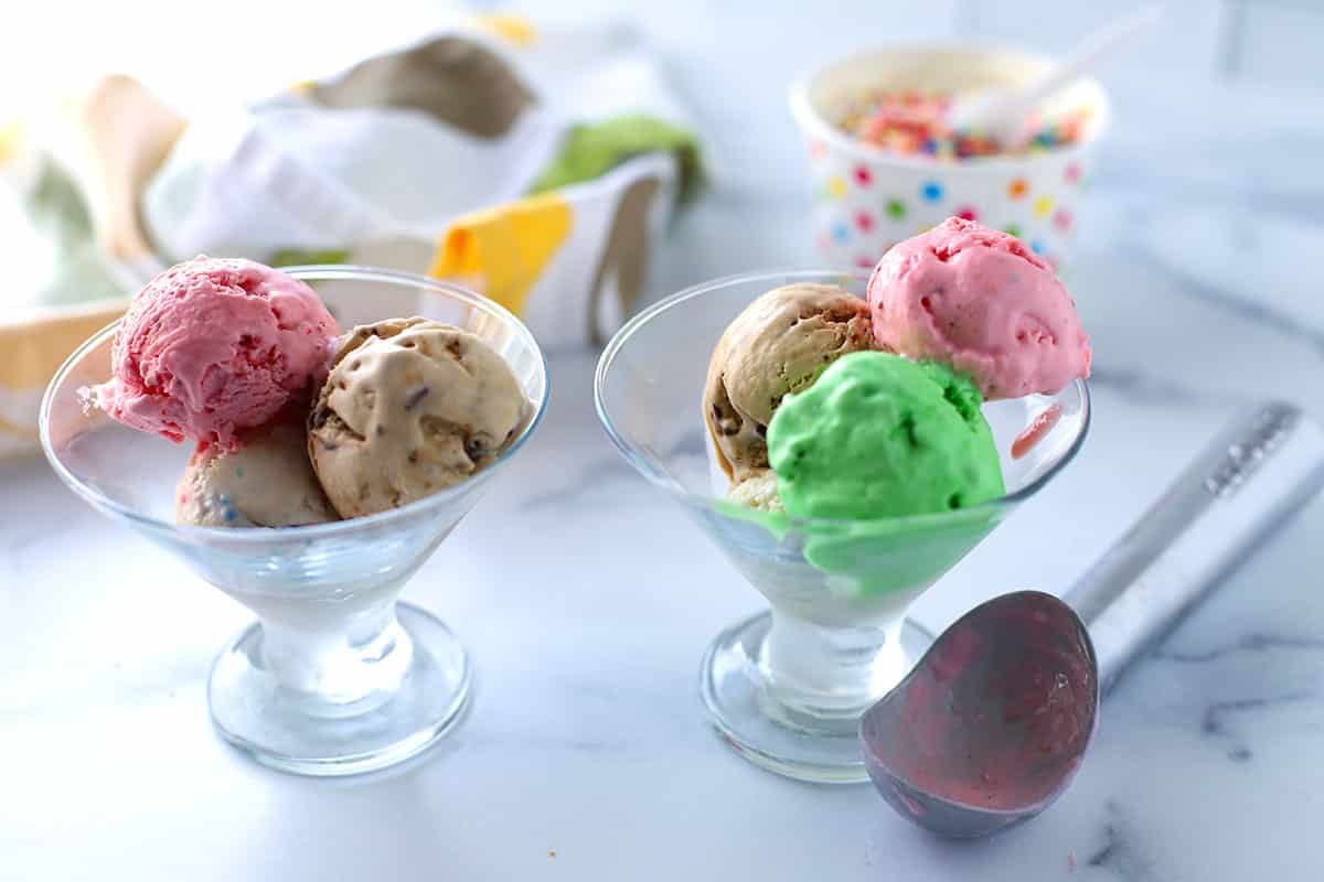 two ice cream glasses with ice cream and an ice cream scoop on the table.