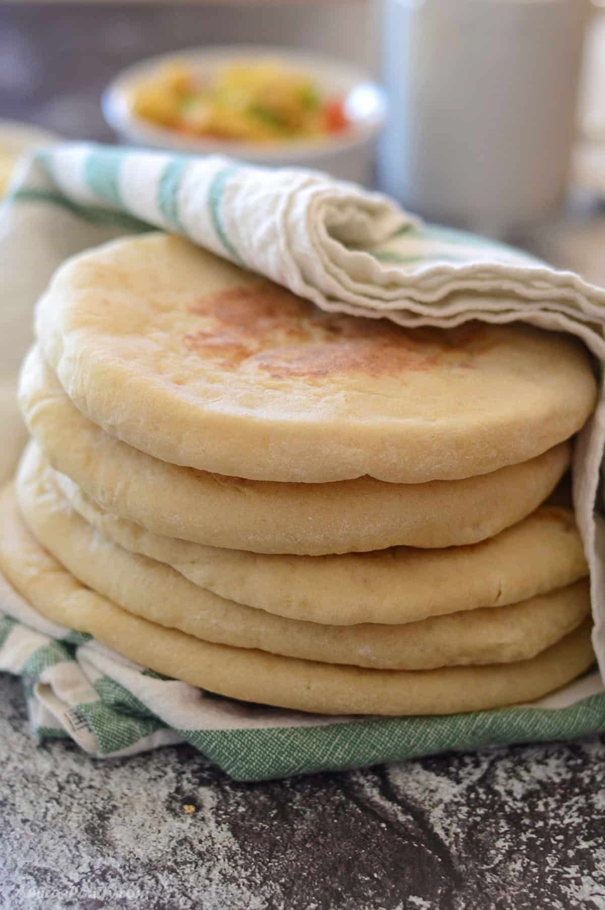 A stack of soft pitas covered with a kitchen towel.