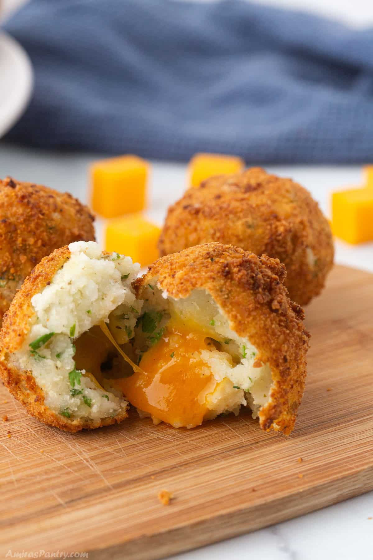 Potato balls on a odden board with one open showing oozing cheese.