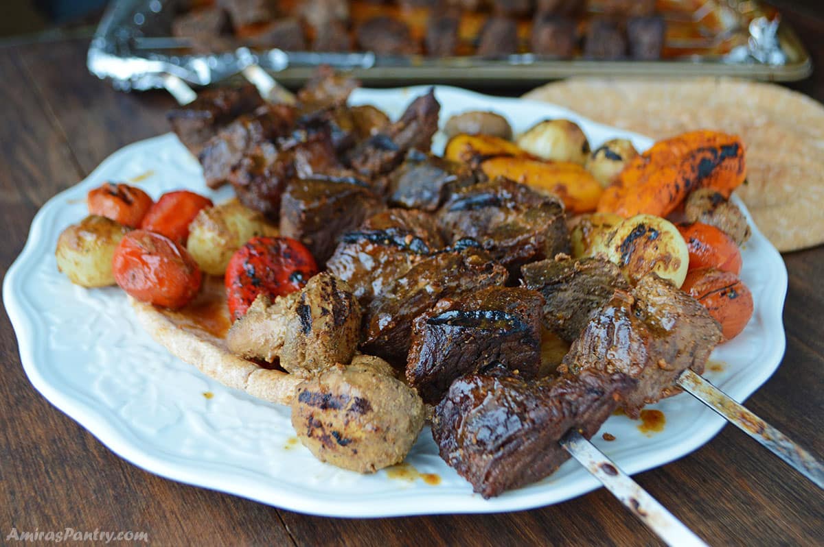 Grilled mushrooms, tomatoes and sweet peppers with shish kebab on a white plate.