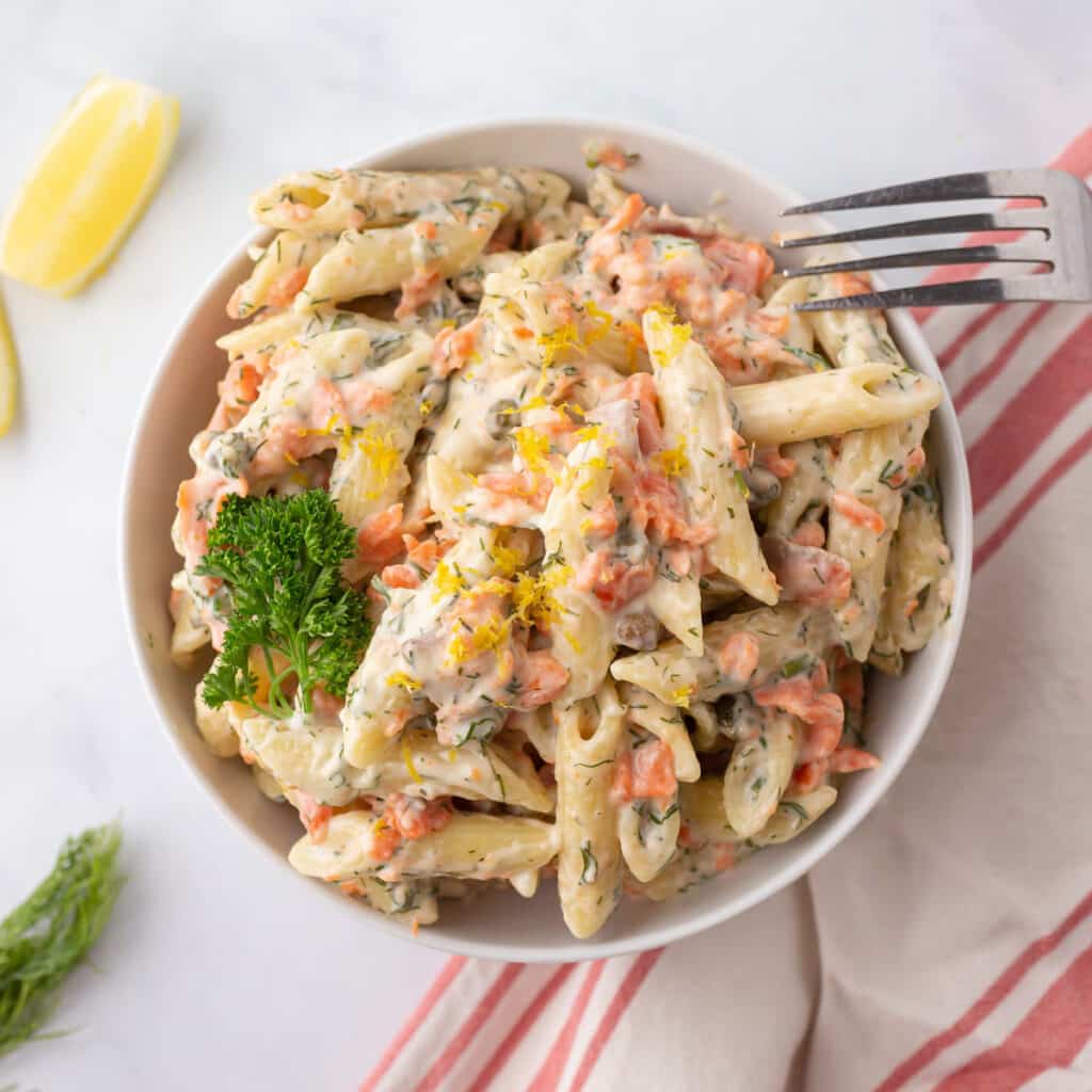 A white bowl with smoked salmon pasta garnished with parsley.