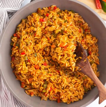 A large skillet of orzo with vegetables and a wooden spoon in it.