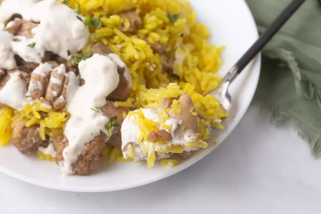 A spoon scooping some shawarma rice from a plate.