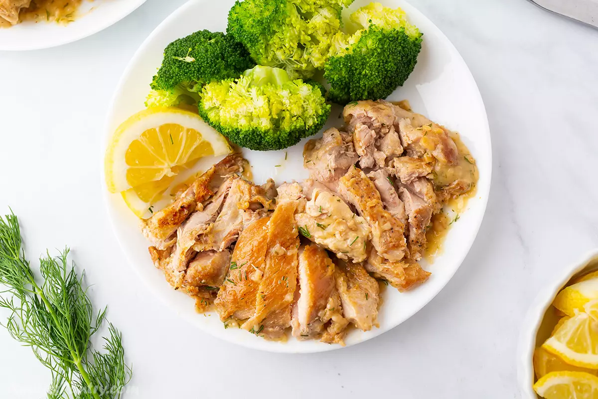 Chicken dill on a white plate with broccoli and a slice of lemon.