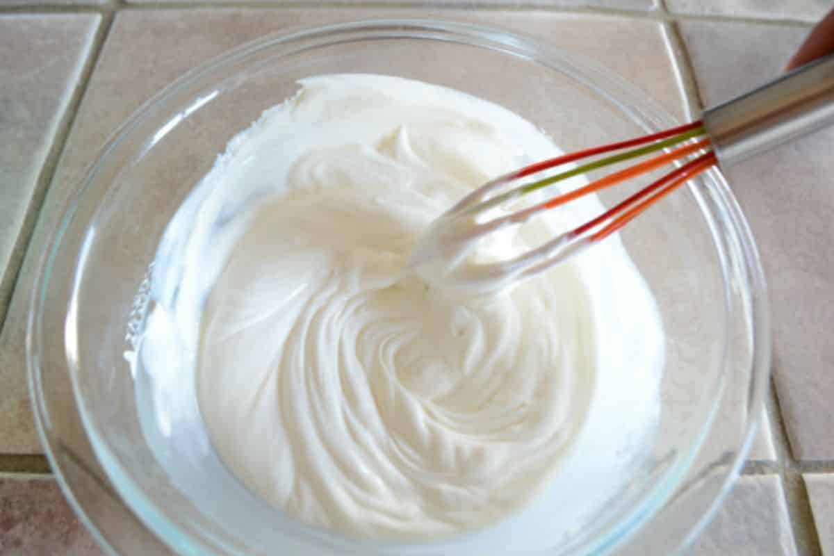 A hand whisking creamy dressing for fruit salad.