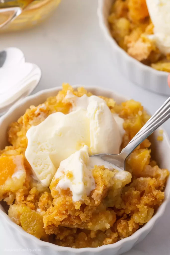 A bowl of peach cobbler with an ice cream scoop on top.