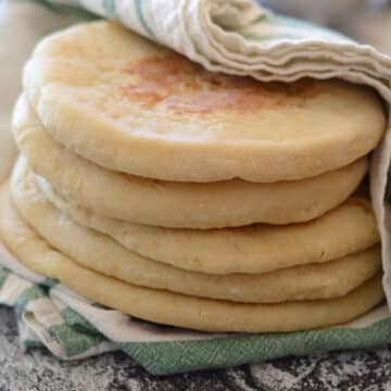 A stack of soft pitas covered with a kitchen towel.