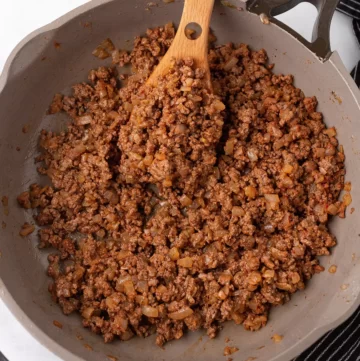 seasoned ground beef in a skillet with a wooden spoon.
