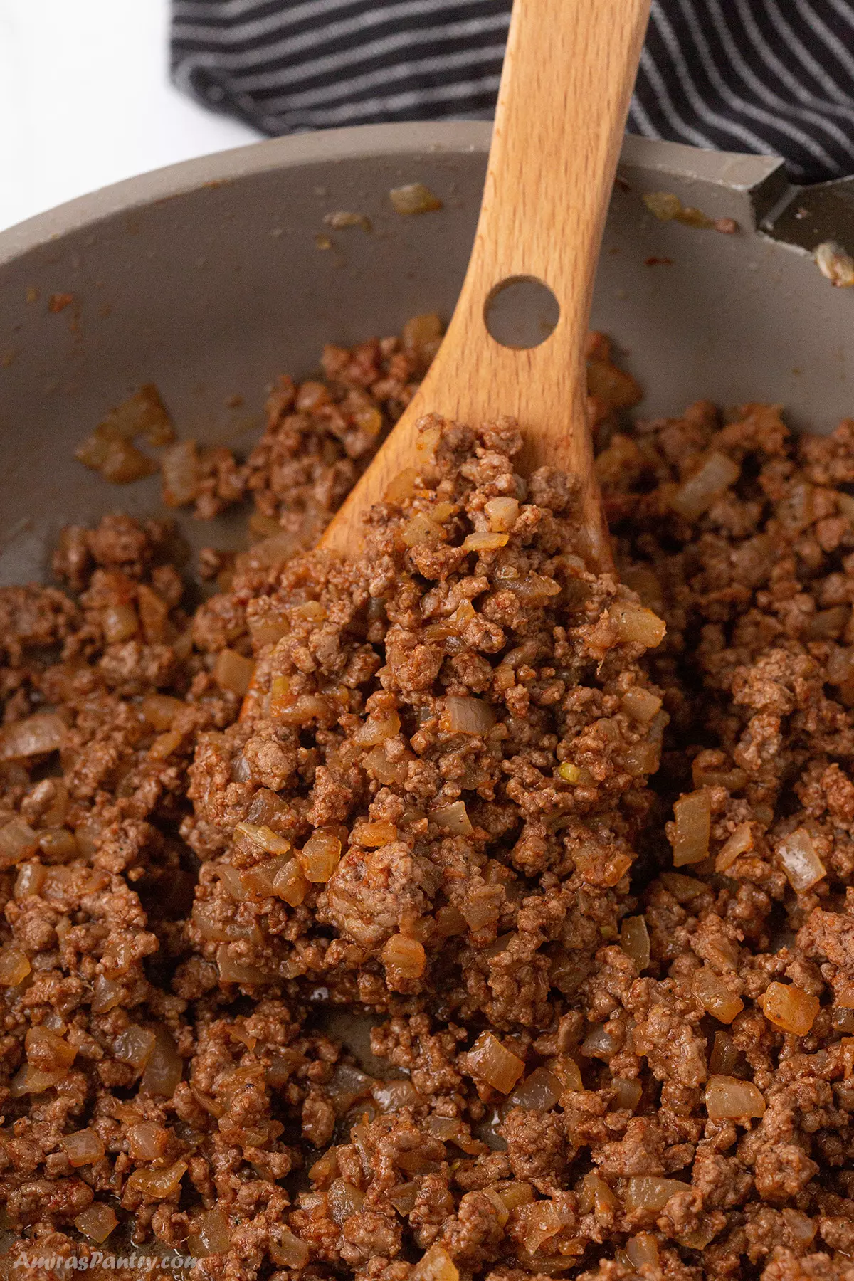 seasoned ground beef in a skillet with a wooden spoon.