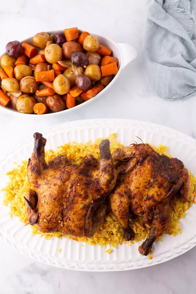 Game hens on a bed of yellow rice on a large white platter.