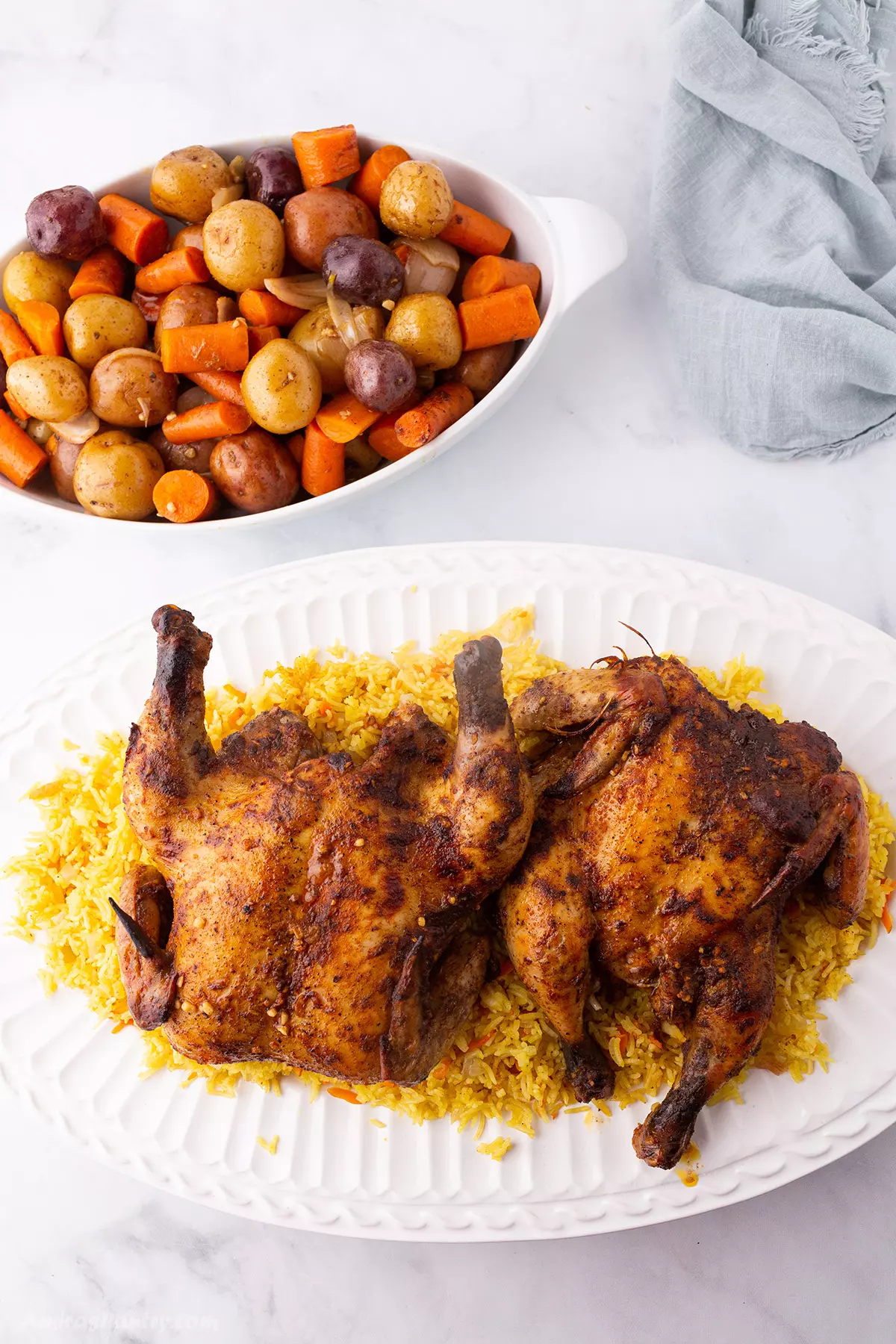 Game hens on a bed of yellow rice on a large white platter.