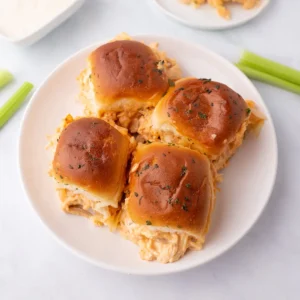 Four buffalo chicken sliders on a white plate.