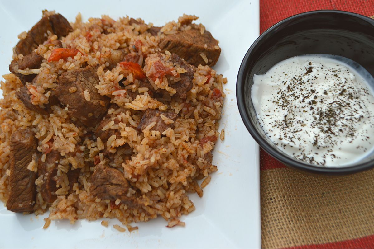 Rice and meat on a white plate with yogurt dip on the side.