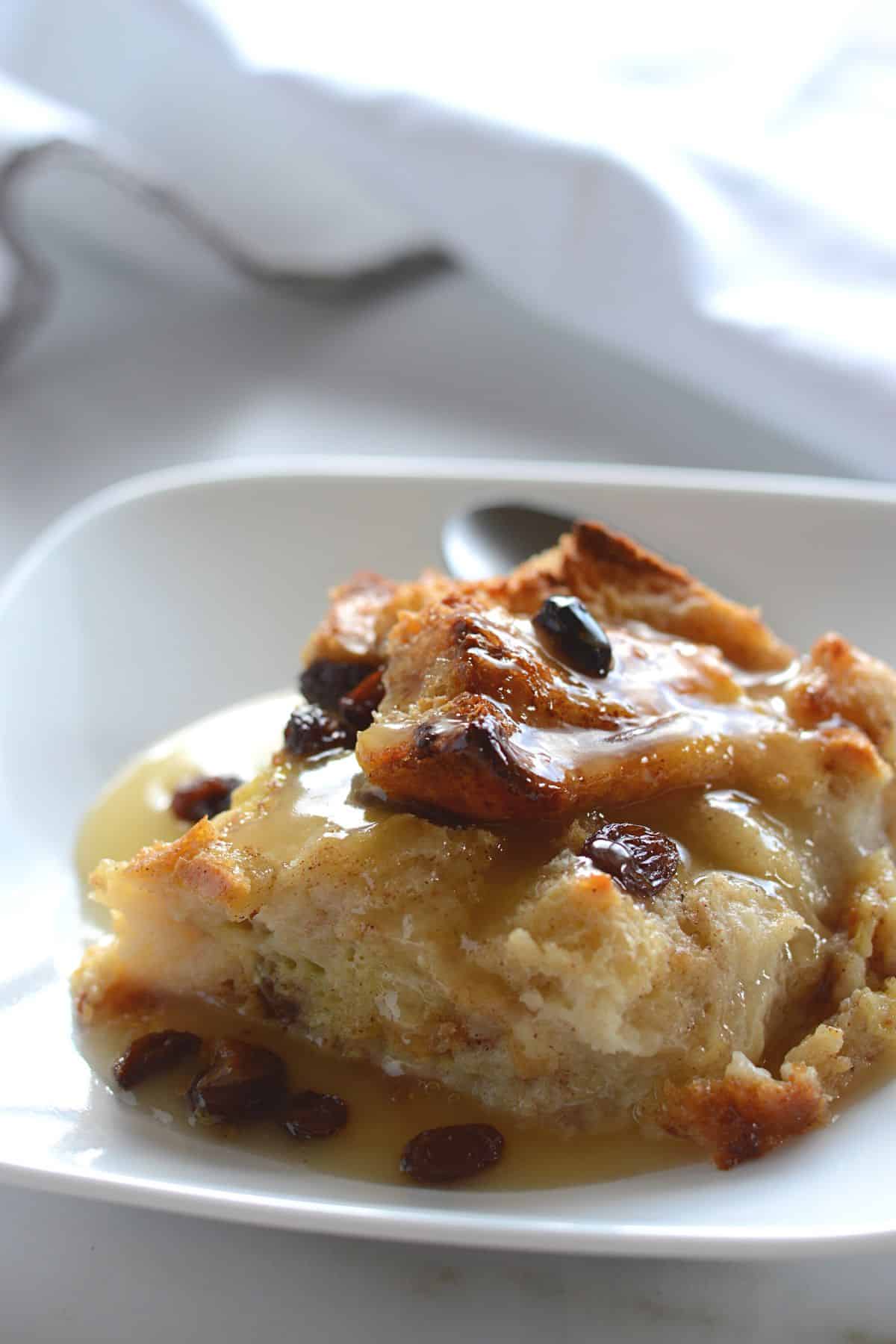 A piece of bread pudding with sauce on a white dessert plate.