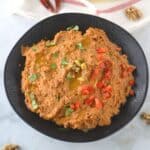 An overhead view of Muhammara on a black plate.