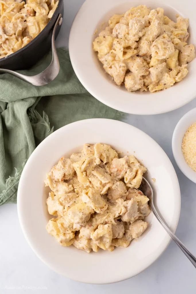 Tortellini Alfredo on a white bowl with a spoon in it.