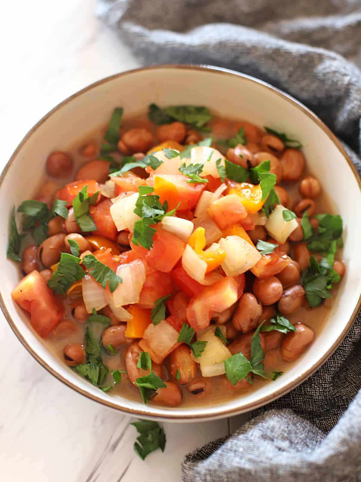 A bowl of ful medames with vegetables.