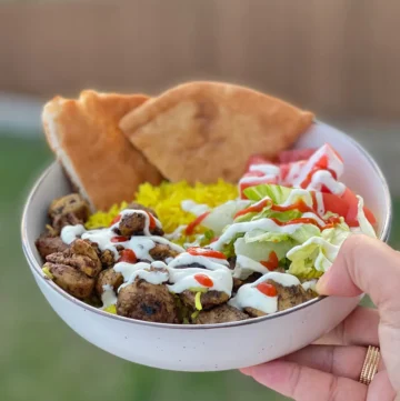 A hand holding a bowl of Halal chicken and rice.