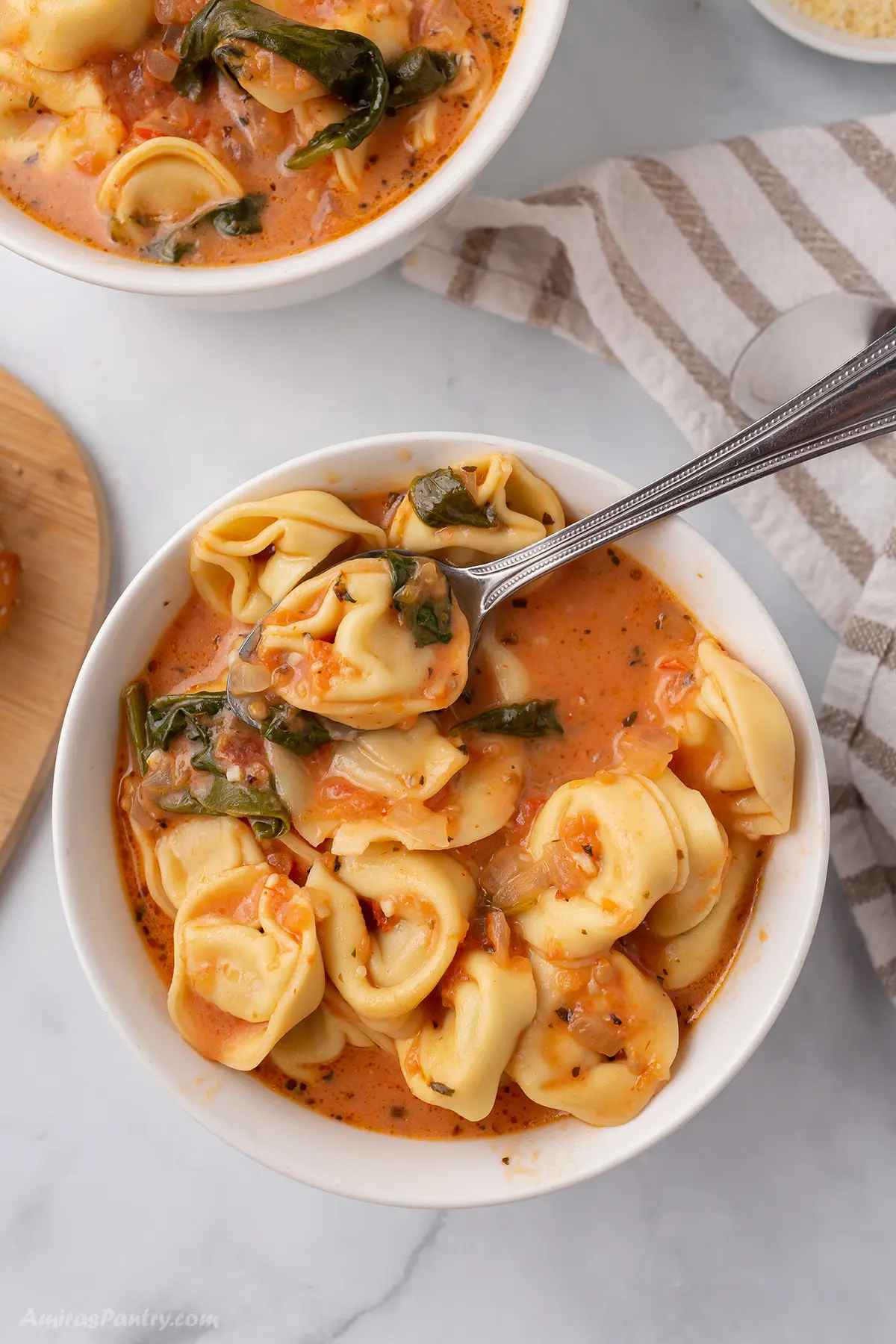 Tortellini soup in white bowls.