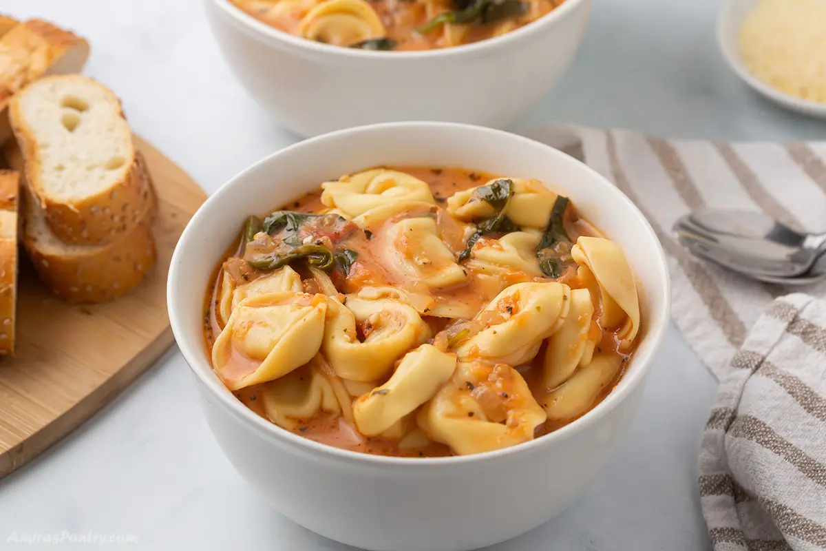 Tortellini soup in a white bowl with another one in the back.