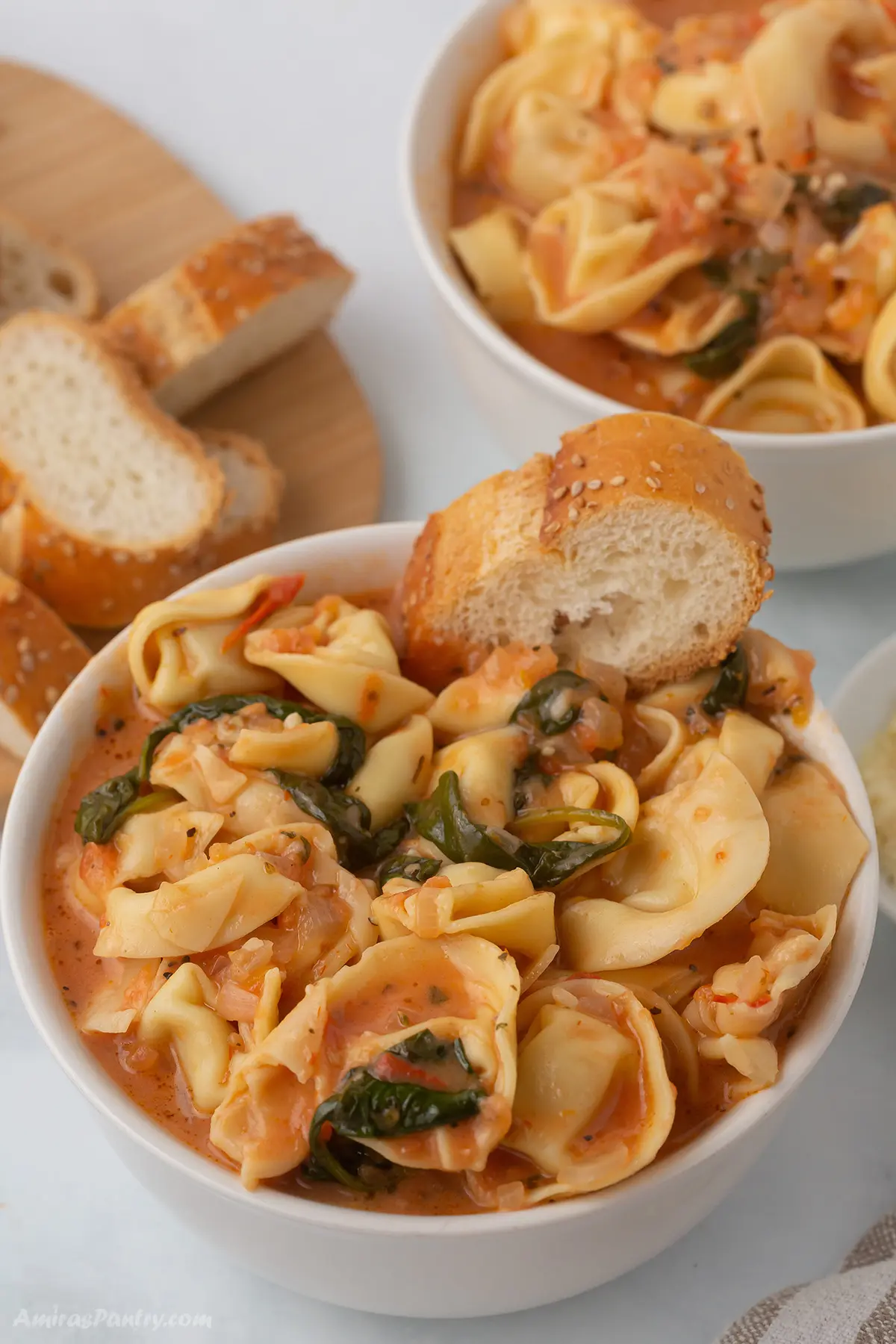A bowl of tortellini soup with a piece of bread in it.