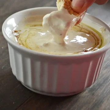 A hand dipping a piece of bread in a bowl of tahini sauce.