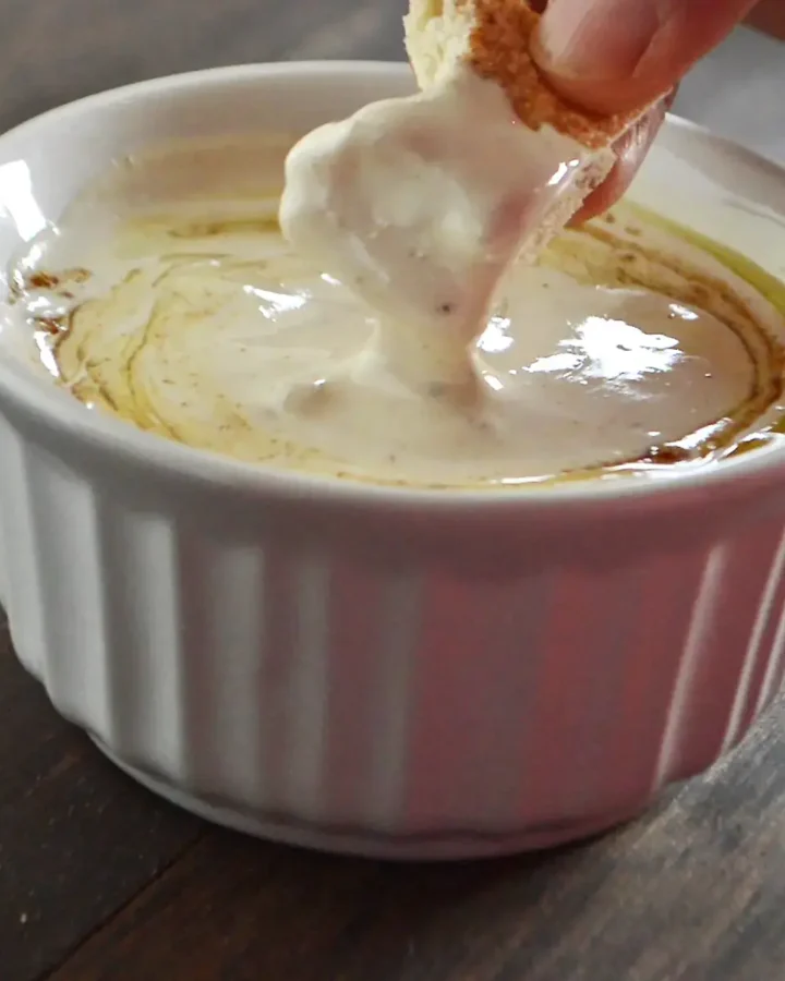A hand dipping a piece of bread in a bowl of tahini sauce.
