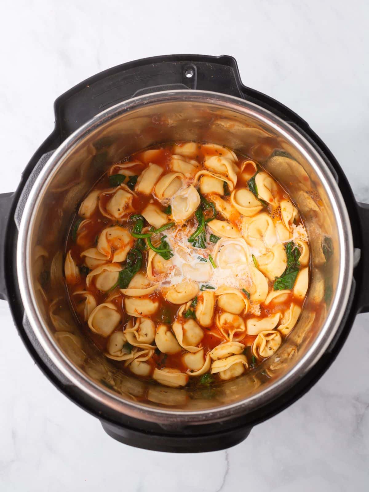 An instant pot with tortellini soup ingredients in it.