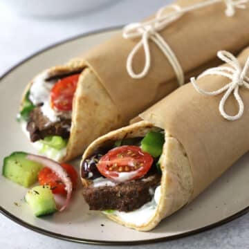 Two gyro wraps on plate with greek salad.