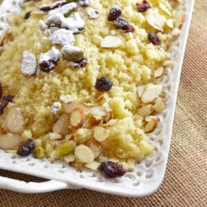 Sweet couscous in a white serving plate garnished with nuts and raisins.