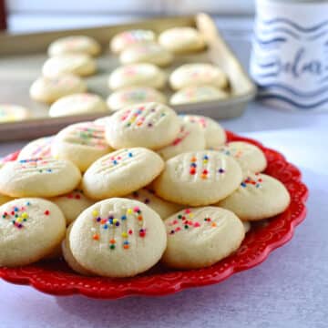 Shortbread cookies on a red plate with the cookie sheet in the background.