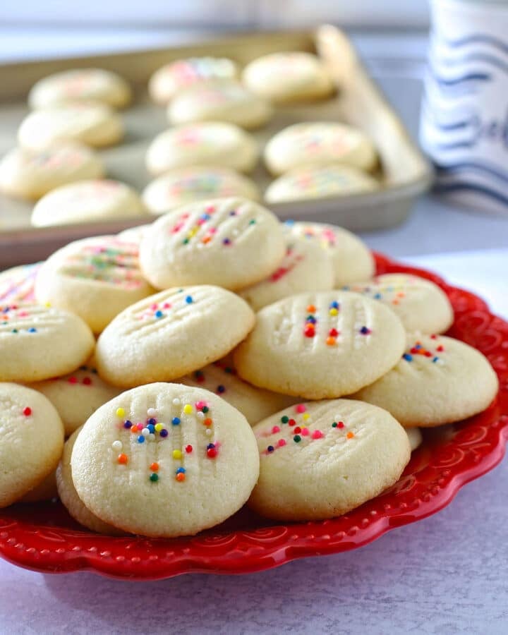 Shortbread cookies on a red plate with the cookie sheet in the background.