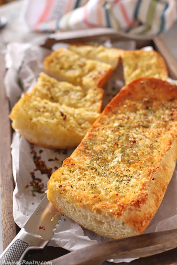Crusty garlic bread on a tray with a knife.