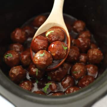 Wooden spoon scooping bbq meatballs out of a slow cooker.