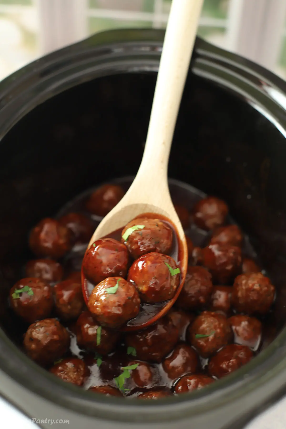 A spoon scooping some bbq meatballs out of a crockpot.